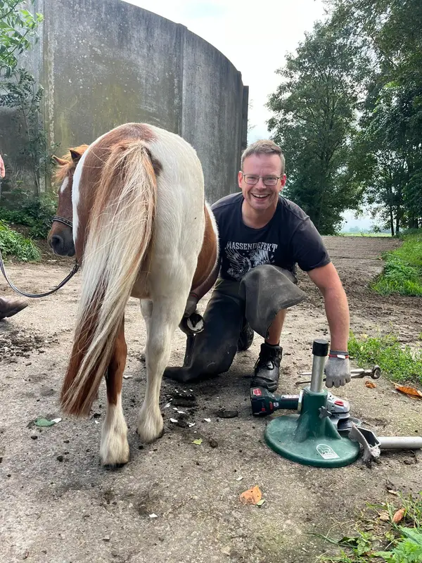 Andre Schnackenberg lächelnd neben einem Schecken-Pony nach dem Beschlag